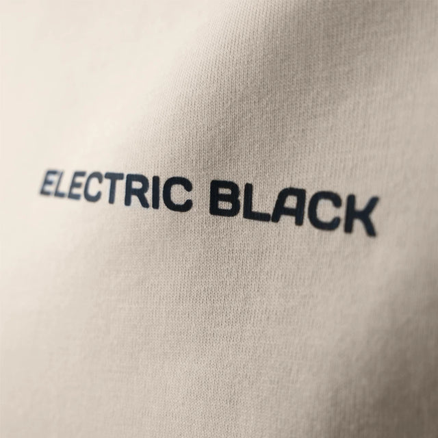 Close-up detail of the beige Electric Black t-shirt, highlighting the logo.
